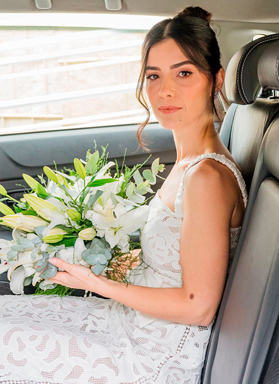 Noiva no carro segurando um buquê de flores brancas